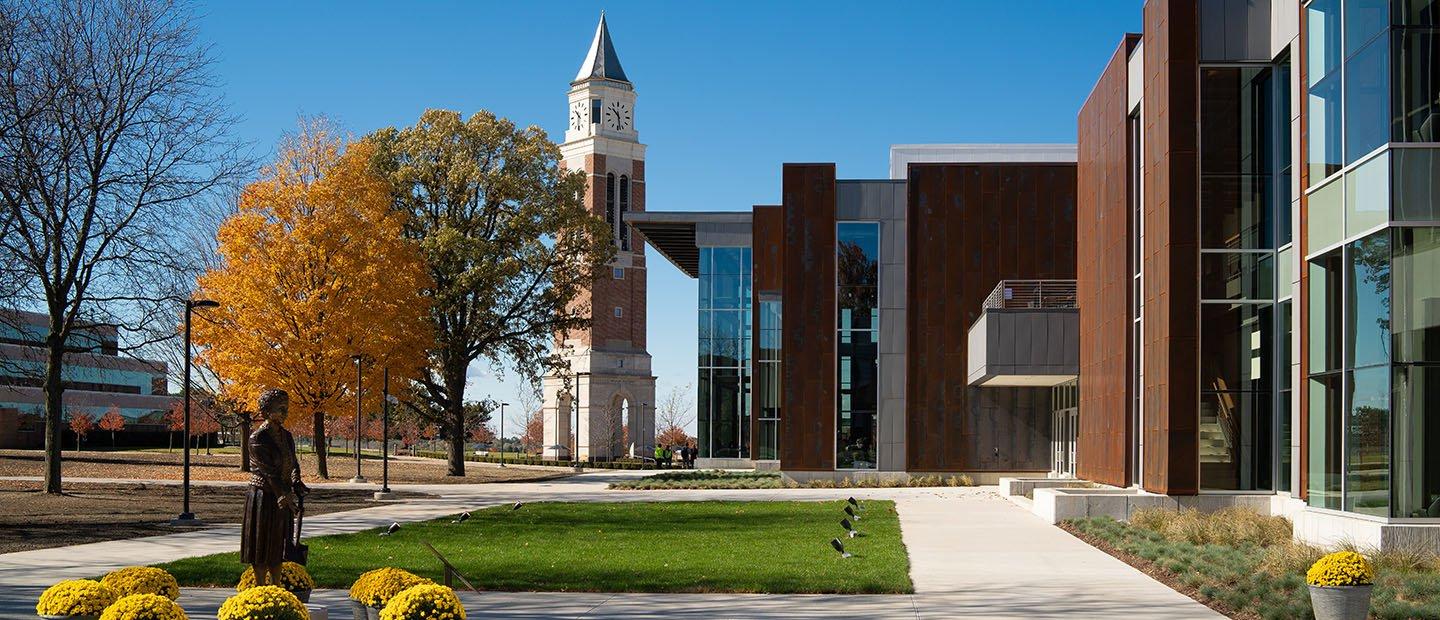 exterior of a brown building with a lot of windows, clock tower in the background