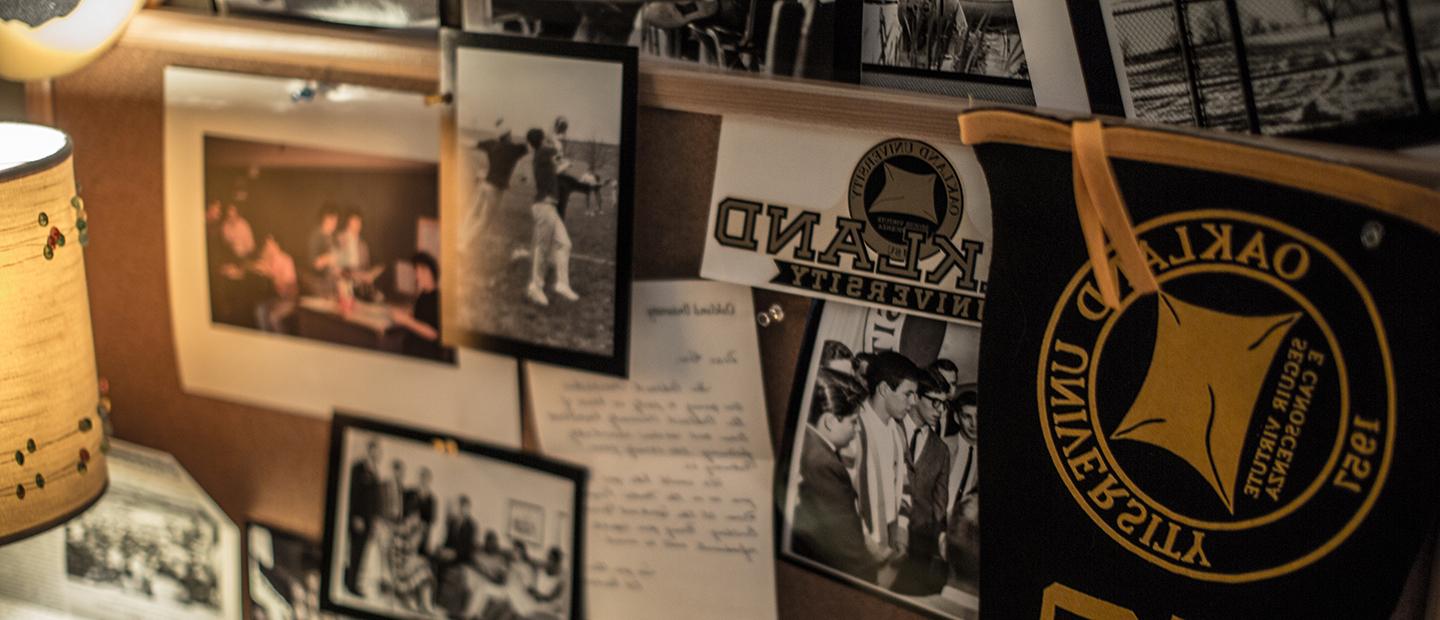 multiple black and white photos and Oakland University memorabilia hanging on a cork board